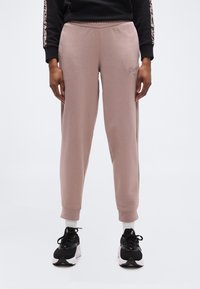 Άτομο που φοράει μοβ παντελόνι φόρμας Puma, λευκές κάλτσες, μαύρα και λευκά αθλητικά παπούτσια Puma, και μαύρο φούτερ με ρίγες λεοπάρ στα μανίκια.