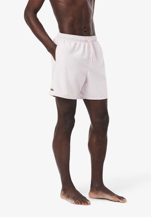 Shorts de bain roses clairs avec taille élastique, cordon de serrage et poches latérales. Présente un petit logo vert sur la cuisse gauche.