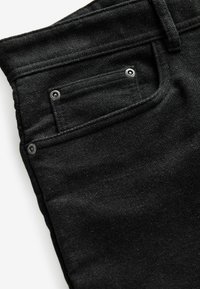 Zwarte jeans met een gestructureerde afwerking, voorzien van een achterzak met zilveren metalen drukknoopdetails en versterkte stiksels.