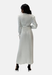 Vestido largo blanco plisado con corpiño ajustado, mangas largas y cinturón en la cintura. Textura lisa con pliegues verticales y falda fluida.