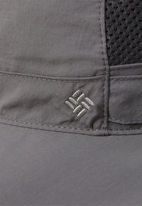 Szürke sapka sima anyagból és hálós panellel. Az elején hímezett logó és figyelemre méltó varrási részletek találhatók.