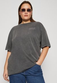 T-shirt de algodón gris de gran tamaño con mangas cortas, que presenta una pequeña estampación blanca que dice "DIVE DEEP INTO SERENITY" en el pecho.