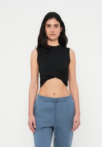 Μαύρο αμάνικο τοπ με σχεδιασμό με κόμπο μπροστά. Συνδυάζεται με μπλε φόρμες, παρουσιάζοντας ένα casual στυλ.