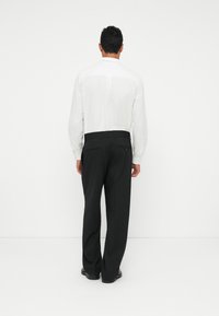 Camisa blanca de manga larga con cuello abotonado, combinada con pantalones negros. Diseño minimalista con textura suave y corte ajustado.