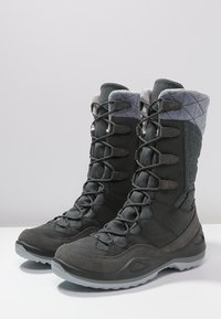 Wysokie szare zimowe buty z pikowanymi kołnierzami, sznurowanymi przodami i grubymi gumowymi podeszwami na białej powierzchni.