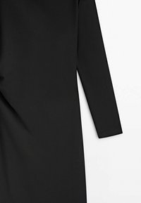 Robe noire à manches longues avec une silhouette ajustée, une coupe droite et un tissu lisse présentée sur fond blanc.