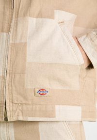 Bežna jakna s patchwork dizajnom v različnih odtenkih, izdelana iz trpežnega materiala. Ima žep s logotipnim oznako na robu.