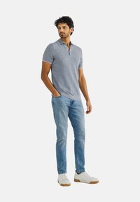 Grijze polo met een twee-knoopsgat, korte mouwen en een contrasterende kraag. Gecombineerd met lichtblauwe jeans en witte sneakers.