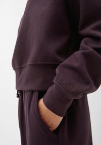 Felpa viola in cotone con design corto, polsini a coste e un logo discreto sulla manica. Tasche laterali per maggiore comodità.