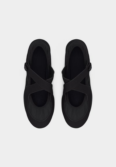 Μαύρα γυναικεία επίπεδα παπούτσια με ελαστικούς λουριά σταυρωτά και στρογγυλεμένες μύτες, εμφανιζόμενα από πάνω προς τα κάτω σε λευκό φόντο.