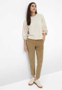 Hellbeige Oversize-Sweatshirt mit Ballonärmeln, kombiniert mit sandfarbenen Cordhosen und beigen Turnschuhen mit einer hellbraunen Sohle.