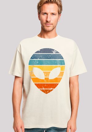 Beige cotton t-shirt featuring a distressed graphic of an alien face in horizontal stripes of blue, teal, yellow, and orange.