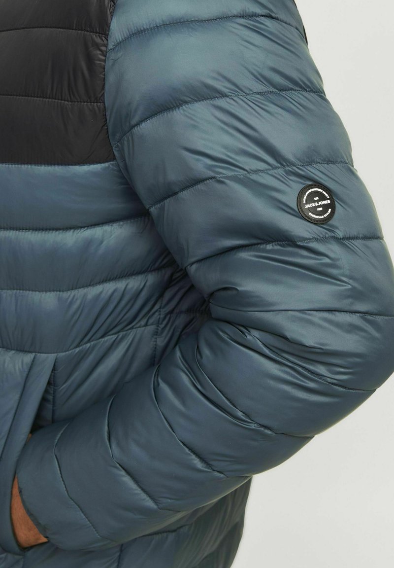 Chaqueta acolchada con un diseño en azul oscuro y negro. Cuenta con un parche de logo en la manga y una textura acolchada horizontal.