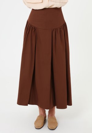 Falda midi marrón de cintura alta con pliegues, combinada con mocasines beige y una camiseta beige metida por dentro, mostrada desde la cintura hasta los pies.