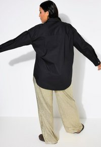 Camisa negra de manga larga con cuello abotonado, de corte relajado. Combinada con pantalones de pierna ancha dorados y texturizados.