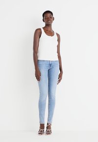 Fehér bordázott ujjatlan top, világoskék slim fit farmernadrág és fehér pántos szandál. Simább szövet, testhezálló fazon és letisztult, minimalista megjelenés.