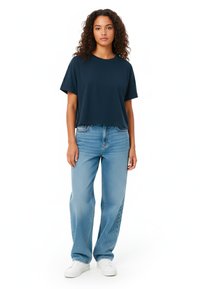 Mornarsko modra kratka majica s kratkimi rokavi, v kombinaciji s svetlo modrimi širokimi kavbojkami in belimi športnimi copati; sproščen kroj in gladka tekstura.