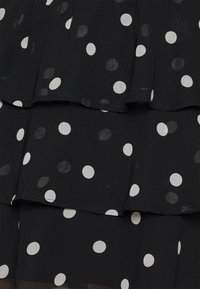 Svart klänning med vita prickar, med lager av volanger. Tillverkad av ett lätt material med en slät yta.