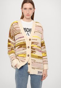 Πολύχρωμο πλεχτό καμπαρντίνα σε κρέμα, με υφασμάτινες ρίγες σε ροζ, κίτρινο και καφέ. Διαθέτει V-λαιμό και μεγάλα καφέ κουμπιά.