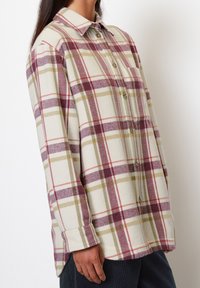 Plaid button-up shirt in cream, burgundy, and olive green. Soft fabric with a relaxed fit and long sleeves. Features a classic collar and buttons.