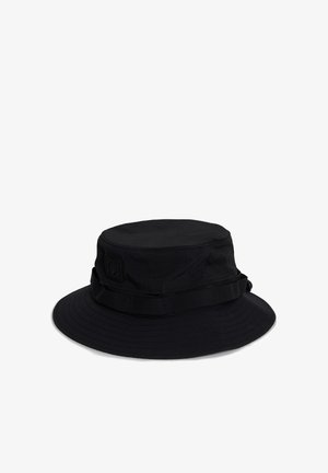 Chapeau bob noir à large bord avec un petit patch logo sur le côté, présenté sur un fond blanc.