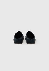 Black suede slip-on shoes featuring a low profile, soft texture, and visible stitching detail along the back and side seams.