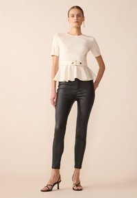 White peplum top with short sleeves and a belt detail; paired with black fitted pants and strappy black high-heeled sandals.
