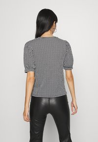 Top s černobílým vzorem houndstooth, krátkými nabíranými rukávy, texturovaným pleteným materiálem a přiléhavým střihem, zkombinovaný s černými kalhotami z umělé kůže.