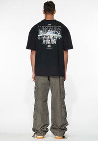 Sort oversized t-shirt med grafikdesign, der viser en bil, parret med grønne cargo-bukser. Casual, afslappet pasform med korte ærmer.