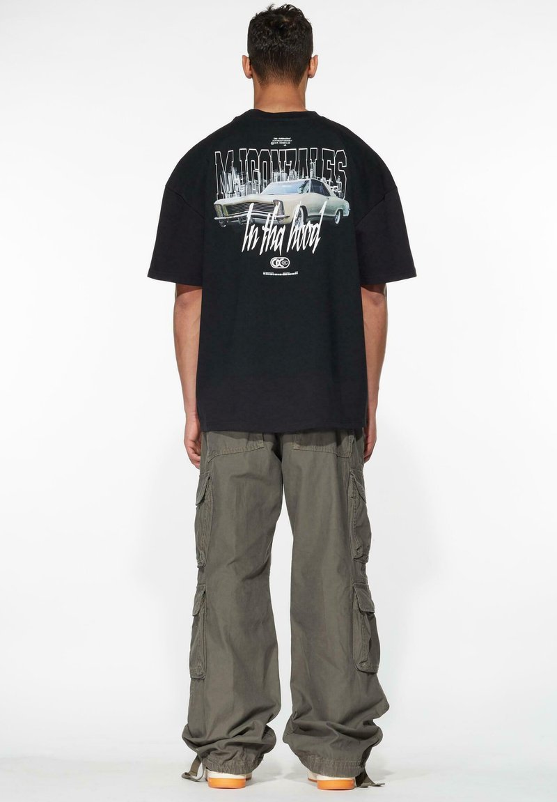 Sort oversized t-shirt med grafikdesign, der viser en bil, parret med grønne cargo-bukser. Casual, afslappet pasform med korte ærmer.