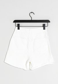 Shorts en denim blanc sur un cintre noir, avec un ourlet replié, deux poches arrière et une texture lisse. Design minimaliste sans motifs.