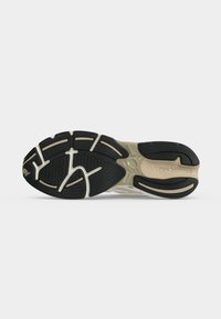 Zool van een beige en zwarte New Balance sneaker met gestructureerde grip-patronen en zichtbaar logo op een effen achtergrond.