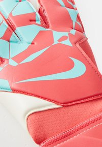 Nike kapus kesztyűk élénkpiros színben, világoskék geometrikus mintákkal. Texturált tapadás, párnázott rész, és fehér díszítés a csuklónál.