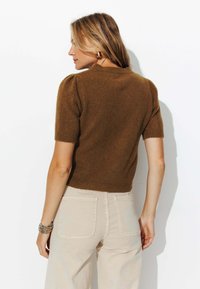 Pull en maille marron à manches courtes avec une coupe ajustée et un tissu texturé, associé à un pantalon taille haute beige clair. Silhouette simple et épurée.