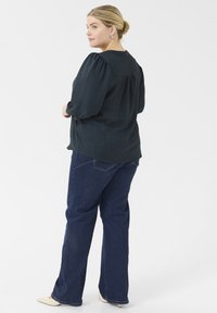 Donkergroene, gestructureerde blouse met pofmouwen, gecombineerd met donkerblauwe flared jeans, gezien van de achterkant. Eenvoudig ontwerp, geen zichtbare patronen.