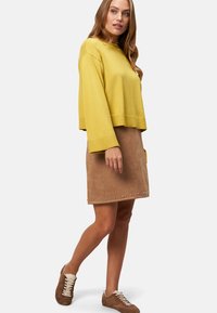 Un pull crop jaune, une jupe en suede beige avec des clous métalliques au bas, et des baskets marron. Textures douces, coupe décontractée.
