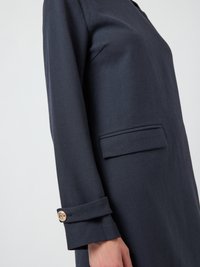 Κοντινό πλάνο ενός ατόμου που φοράει ένα σκούρο ναυτικό σακάκι με τσέπη flap και χρυσή λεπτομέρεια στο μανίκι.