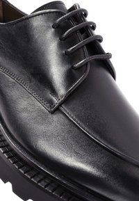 Schwarzer Lederschuh mit glatter Oberfläche, Schnürdesign und auffälliger Naht. Verfügt über eine dicke, strukturierte schwarze Außensohle.