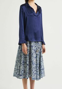 Blusa lunga in satin blu navy con scollo a V e maniche a campana, abbinata a una gonna blu con stampa floreale, dotata di pieghe e orlo con ruches.