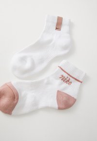 Chaussettes blanches à la cheville avec une texture côtelée, présentant un accent rose au niveau du talon et une bande logo rose en haut.
