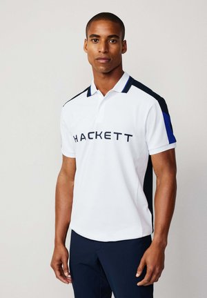 Hvid polo shirt med marineblå og blå sidepaneler samt et "HACKETT" logo på brystet. Korte ærmer og klassisk kravedesign.