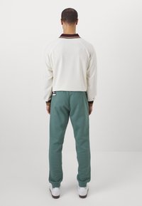 White fleece pullover with maroon collar and brown accents, paired with teal sweatpants, featuring a relaxed fit and white sneakers.