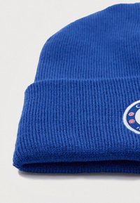 Zils beanie cepure, izgatavota no ribota adījuma auduma. Izkļautina apaļa, izšūta uzlīme ar logo. Ar apmali un mīkstu tekstūru.