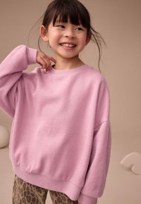 Svetloružová nadrozmerná mikina s rebrovanými manžetami a lemom, vyrobená z mäkkého materiálu; kombinovaná so legínami so zvieracím vzorom.