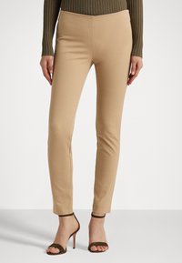 Tan färgade tighta byxor med en slät textur, som har hög midja och raka ben, i kombination med bruna klacksandaler.