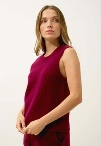 Burgundy ärmlös stickad topp med ribbat mönster, rund halsringning och avslappnad passform, bärs över matchande burgundy byxor.