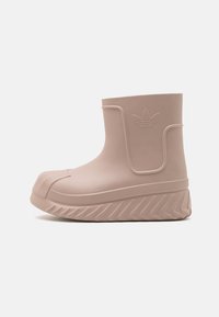 Bota de goma de color rosa pálido con punta redondeada, logotipo grabado, suela texturizada y tacón pronunciado. Diseño sencillo con superficie lisa y acentos mínimos.