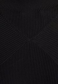 Svart ribbad tyg med hög krage och ett distinkt korsstygnsmönster på baksidan. Texturerad, figurnära design.