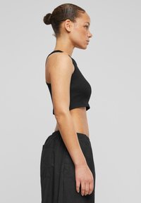 Must mustriba, lühikeste varrukatega must crop top, paaritatud kergete mustade pükstega, millel on küljetaskud. Sile tekstuur, vormiv disain.
