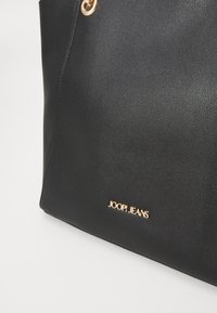 Czarna skórzana torba typu tote z złotymi akcentami, z wytłoczonym logo "JOOP! JEANS" z przodu i gładką teksturą.